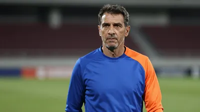 Middle-aged, athletic manager with short dark hair, focused eyes, slight stubble, wearing a plain, unmarked training top...