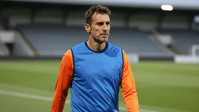 A medium shot of a middle-aged, athletic-build man in his mid-40s, dressed in a plain blue training top with orange...