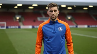 A determined, mid-20s, athletic Latics midfielder with a strong build, wearing a plain blue and orange training top...