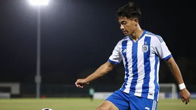 A 23-year-old midfielder in a blue and white striped kit, with a white shirt and blue shorts, playing a pass on the...