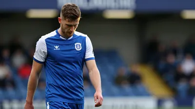 A tight, waist-up shot of an Oldham Athletic player in a blue shirt with white sleeves, looking dejected as he walks off...