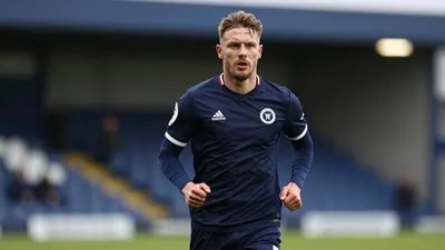 A 30-year-old Oldham Athletic midfielder in navy blue kit, waist-up, running onto the pitch at an away ground