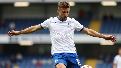 A 30-year-old Oldham Athletic player in a white jersey with a blue collar, a blue number 10 on the back, and a blue pair...