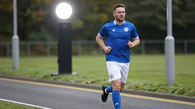 A photorealistic image of an anonymous Oldham Athletic staff member, aged 30-40, wearing a blue jersey and white shorts...