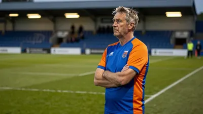 A 35-year-old, ruggedly-built, assistant coach with a weathered face and wisps of grey hair, stands intensely on the...