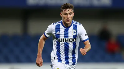A 25-year-old Oldham Athletic midfielder, wearing a blue and white striped kit, runs with the ball, his face set in...