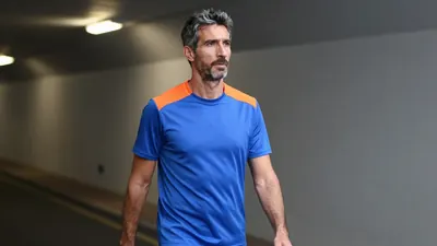 A tight, waist-up shot of a 35-year-old, 5'10" Oldham player, dressed in a plain blue and orange crew-neck training top...