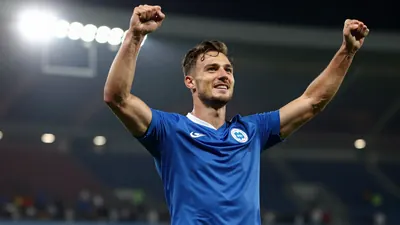 A muscular 29-year-old wing-back in a solid blue kit, celebrating a goal with arms raised