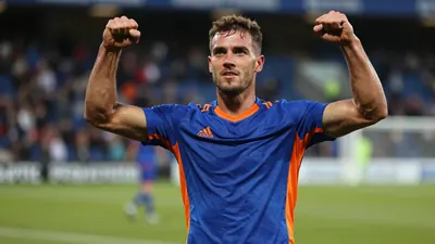 Mid-30s muscular Oldham midfielder, waist-up, face intense and eyes sharp, celebrating a goal with arms raised, sweat...