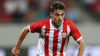 A 24-year-old winger in a red and white striped jersey, mid-dribble, with a focused expression