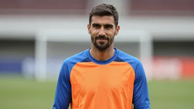 Mid-30s male football manager, athletic build, waist-up, wearing a plain, unmarked training top split blue and orange...