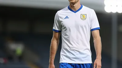 A 30-year-old centre-back in a white Oldham Athletic shirt, made of smooth cotton, with a bright blue collar and sleeves...