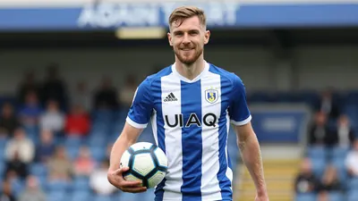 A photorealistic image of an Oldham Athletic player, aged 25-30, wearing a blue and white striped kit, natural light, and...