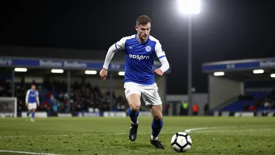 A 30-year-old Oldham Athletic midfielder, wearing a blue jersey with white sleeves, and white shorts, and black boots...