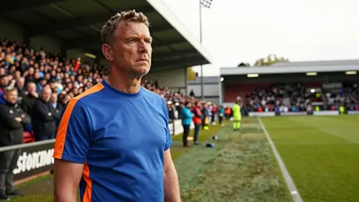A 35-year-old, ruggedly-built, Oldham Athletic coach, wearing a plain blue and orange polyester training top, stands at...