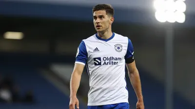 A 30-year-old Oldham Athletic player, with a medium build, in a blue and white kit, photographed with an 85mm f/1.4 lens...