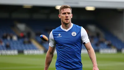 A photorealistic image of an Oldham Athletic player, wearing a blue shirt with white sleeves and a white collar, looking...