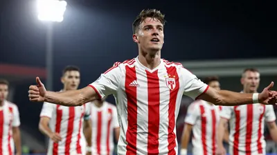 A 28-year-old midfielder in a red and white striped kit, waist-up shot, celebrating a goal with teammates blurred in the...